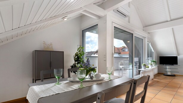 Un comedor con una mesa dispuesta para dos, una planta y un televisor al fondo.