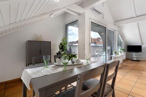 A dining area with a table set for two, a plant, and a television in the background. - Apartment 'Sämann' with Mountain View, Balcony and Wi-Fi (Oberkirch)