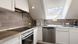 Una cocina moderna con armarios blancos, horno empotrado, lavavajillas y tragaluces.