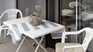 Mesa y sillas blancas en un patio con mantel a rayas, una cesta tejida y un cojín en la silla.