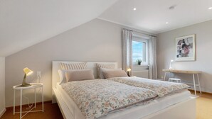Un dormitorio con cama, mesitas de noche, escritorio y ventana.