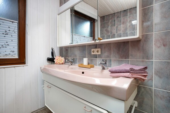 A bathroom with a sink, mirror, window, and tiled walls.