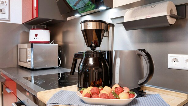 Une cuisine équipée d’une machine à café, d’un four à micro-ondes, d’un grille-pain et d’un saladier rempli de fruits, posé sur le plan de travail.