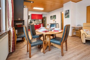 A dining area with a round table, four chairs, and a kitchen in the background.