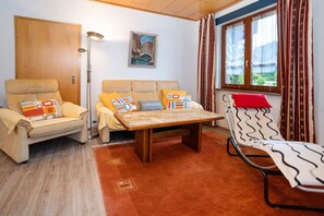 A room with a sofa, a recliner, a table, and a window with curtains.