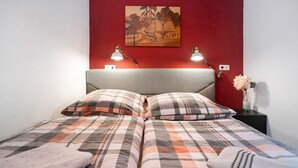 Un lit avec une couette à carreaux, deux lampes de chevet, un mur rouge et un tableau au-dessus du lit.
