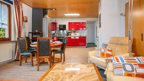 Un salon avec un canapé, une table à manger entourée de chaises, une cuisine à l’arrière-plan et une fenêtre avec des rideaux.