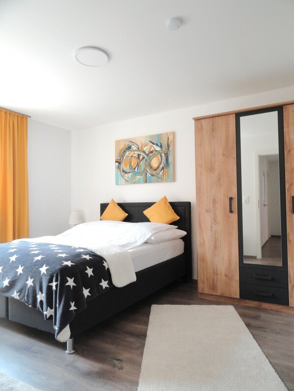 A modern bedroom with a bed, a wooden wardrobe, a mirror, and a ceiling light.