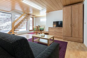 Uma sala de estar moderna com escada de madeira, sofá, mesa de centro e televisão.