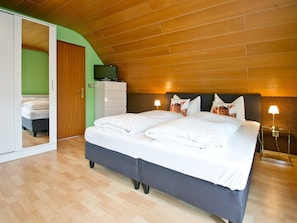 Un dormitorio con cama, televisor sobre una cómoda, mesita de noche con lámpara y espejo.