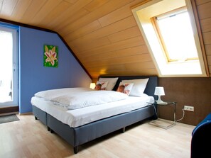 Une chambre avec un plafond en pente, un lit avec une literie blanche, une table de chevet avec une lampe et une fenêtre.