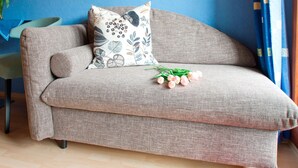 A sofa with a patterned cushion, a vase with flowers, and a blue wall. - Room 'Julia' with Shared Terrace, Balcony and Wi-Fi (Bad Rippoldsau-Schapbach)