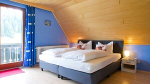 A bedroom with a bed, a nightstand, a window with curtains, and a view of the outdoors. - Room 'Julia' with Shared Terrace, Balcony and Wi-Fi (Bad Rippoldsau-Schapbach)