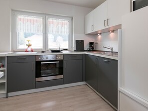 Eine moderne Küche mit grauen Schränken, einem Einbauofen, einer Kaffeemaschine und einem Fenster mit Vorhängen.