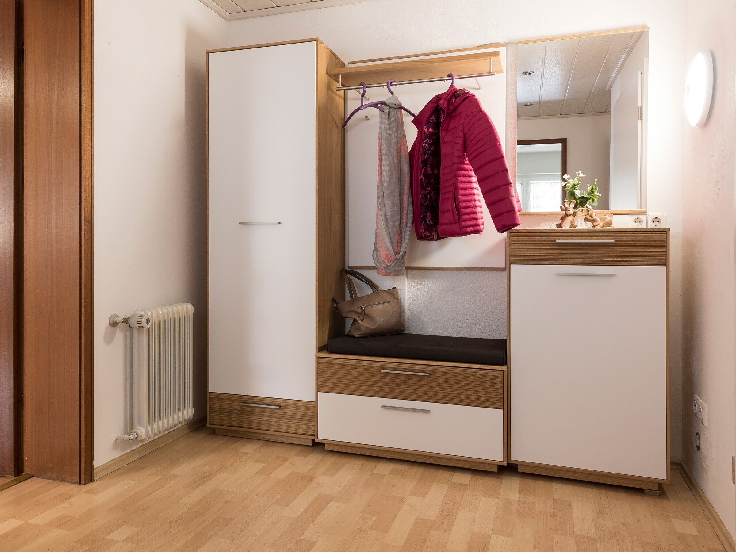 Ein Zimmer mit Schrank, Sitzbank, Spiegel und Heizkörper.