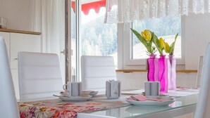 A dining area with a glass table, white chairs, a floral tablecloth, and a window with a view of trees. - Apartment 'Rosi Mit 80qm' with Shared Terrace, Balcony and Wi-Fi (Bad Rippoldsau-Schapbach)