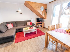 Un salon comprenant un canapé, une table basse, un meuble pour la télévision, une table à manger et un tapis rouge.