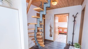 Une pièce avec un escalier en bois, un lit, une table avec une plante et un porte-manteau.