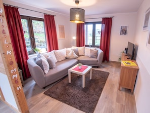 A modern living room with a grey sectional sofa, a wooden coffee table, a red rug, and a TV on a wooden stand. - Ferienhof Pulte Apartment "Haferkiste" with Mountain View, Shared Terrace, and No Wi-Fi (Attendorn)