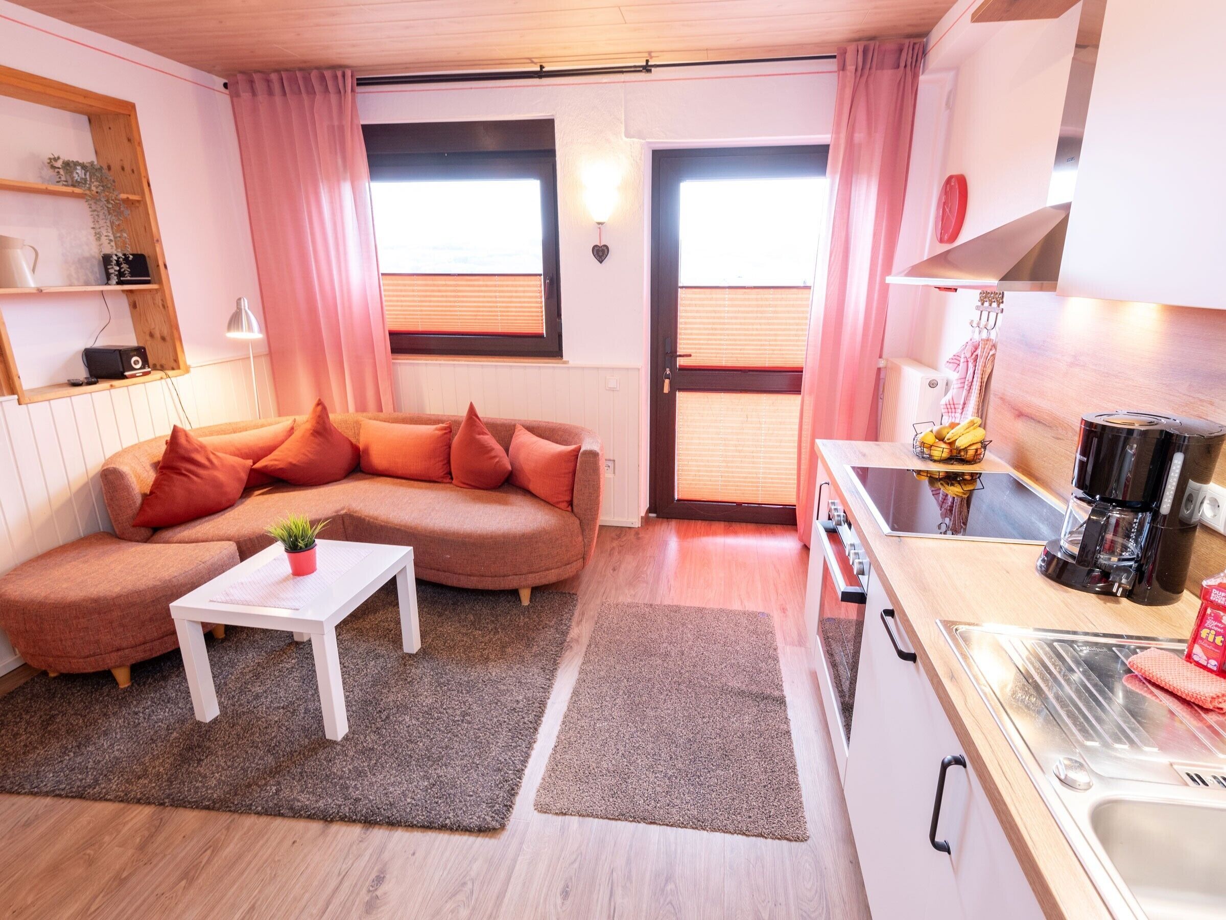 Ein kompakter Wohnbereich mit einer Couch, einem kleinen Tisch, einer Kaffeemaschine und einer Küchenzeile.