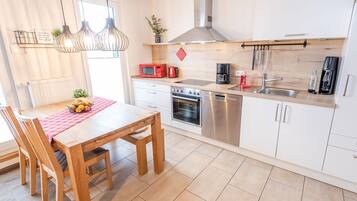 A modern kitchen with white cabinets, stainless steel appliances, a wooden dining table, and pendant lighting.