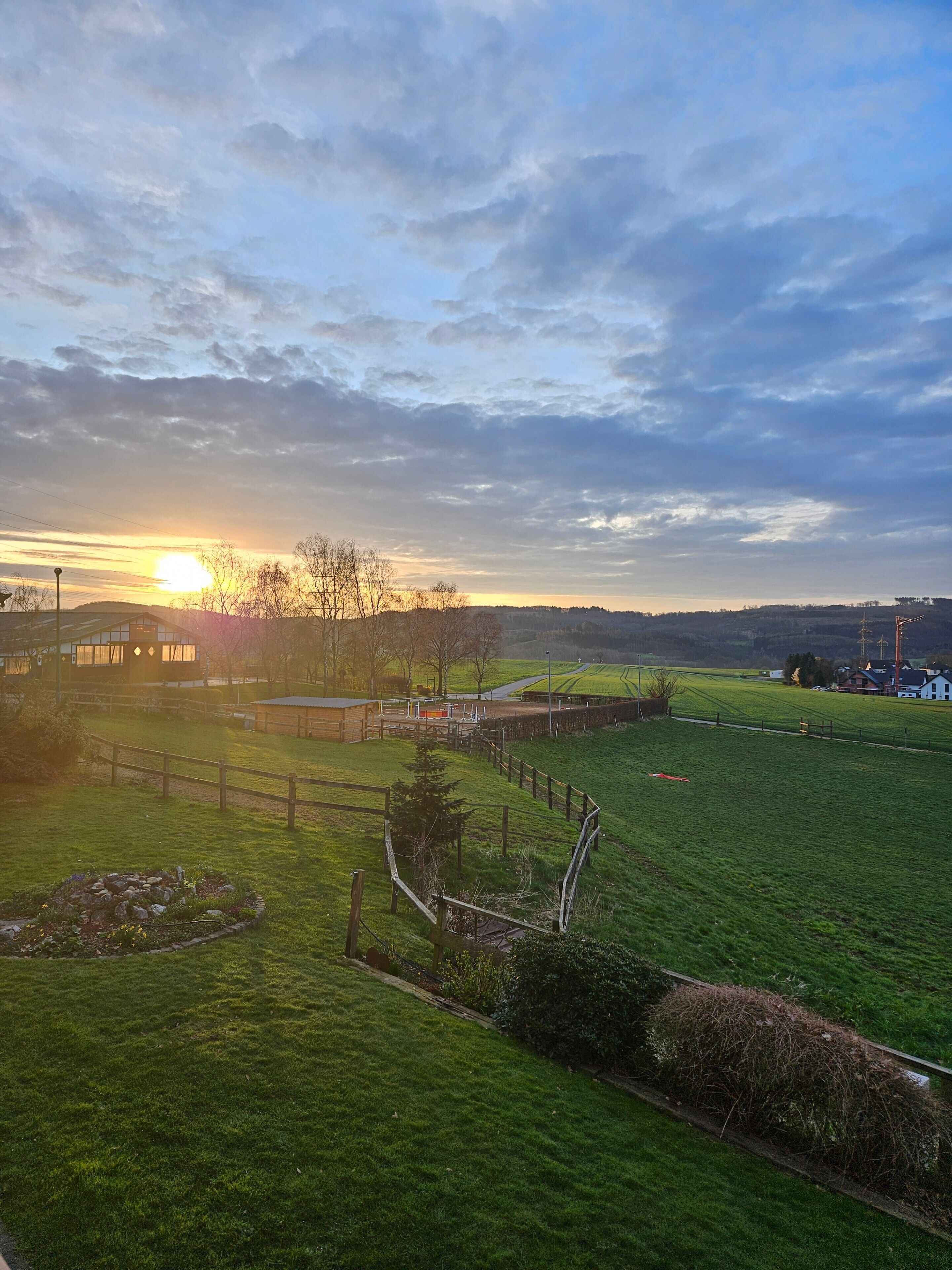 A rural landscape with a sunset, open fields, and a distant building.