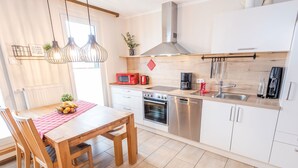 A modern kitchen with white cabinets, stainless steel appliances, a wooden dining table, and pendant lighting. - Holiday Apartment 'Gänseblümchen' with Mountain View, Shared Terrace and Wi-Fi (Attendorn)