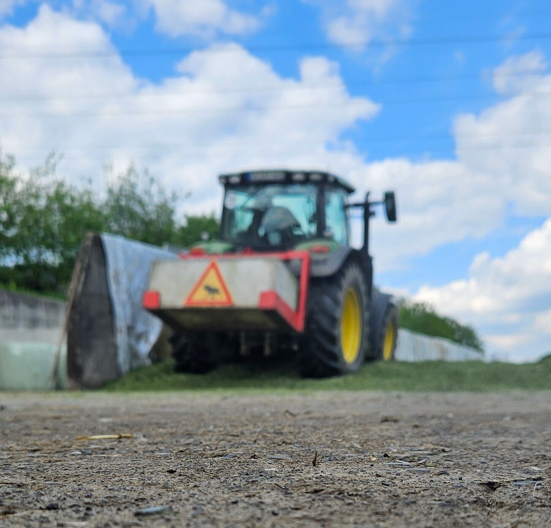 A tractor on a dirt road with a blue sky and clouds in the background.