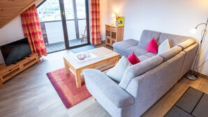 A living room with a sofa, a coffee table, a TV on a stand, a small wooden cabinet, and a view through a large window. - Holiday Apartment 'Gänseblümchen' with Mountain View, Shared Terrace and Wi-Fi (Attendorn)
