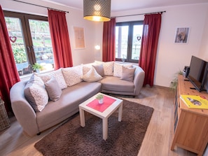 A living room with a sofa, a coffee table, a TV, and a window with curtains.