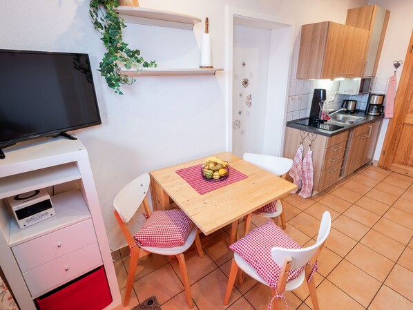 A compact kitchen with a dining area, a television, and a small cabinet.