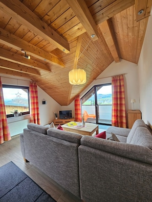 Una sala de estar acogedora con techo de madera, un sofá, un televisor y vistas al exterior.