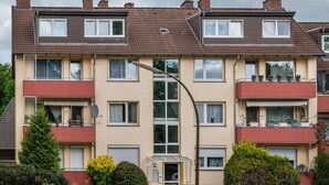Un edificio residencial de varios pisos con balcones, una antena parabólica y plantas en macetas.