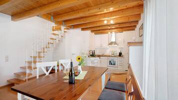Una cocina moderna con armarios blancos, una mesa de comedor de madera y una escalera que sube a un nivel superior.