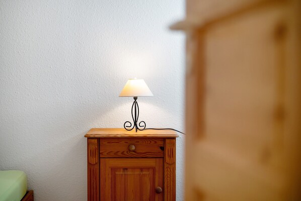 Ein Nachttisch aus Holz mit einer Lampe, ein grüner Stuhl und eine weiße Wand.