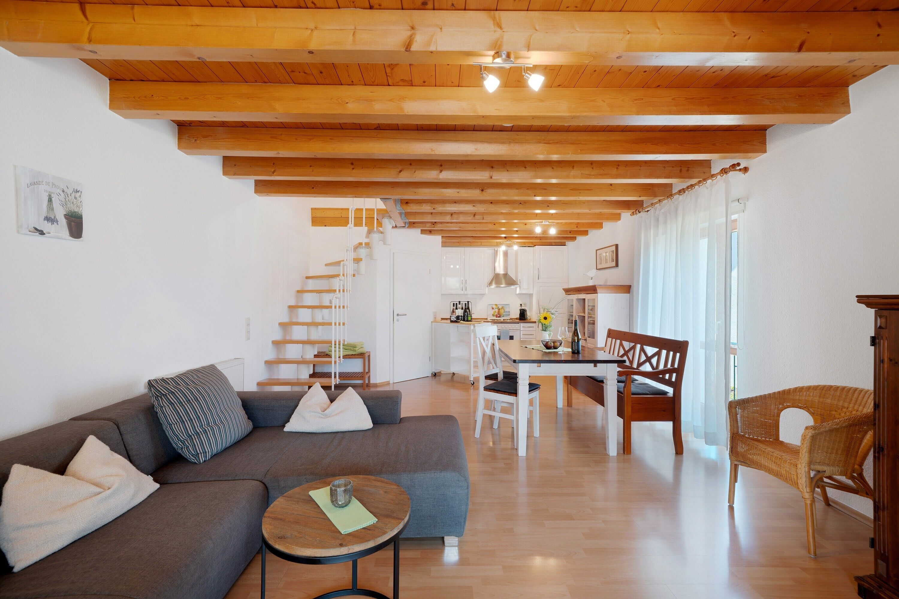 A modern living room with a sofa, a dining table, and a staircase leading to a kitchen.