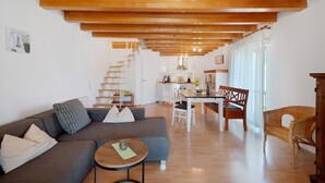 A modern living room with a sofa, a dining table, and a staircase leading to a kitchen. - Apartment '2, 65 Qm, Balkon' with Shared Pool, Private Terrace and Wi-Fi (Vogtsburg)