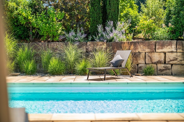 A poolside area with a lounge chair, a stone wall, and various plants.