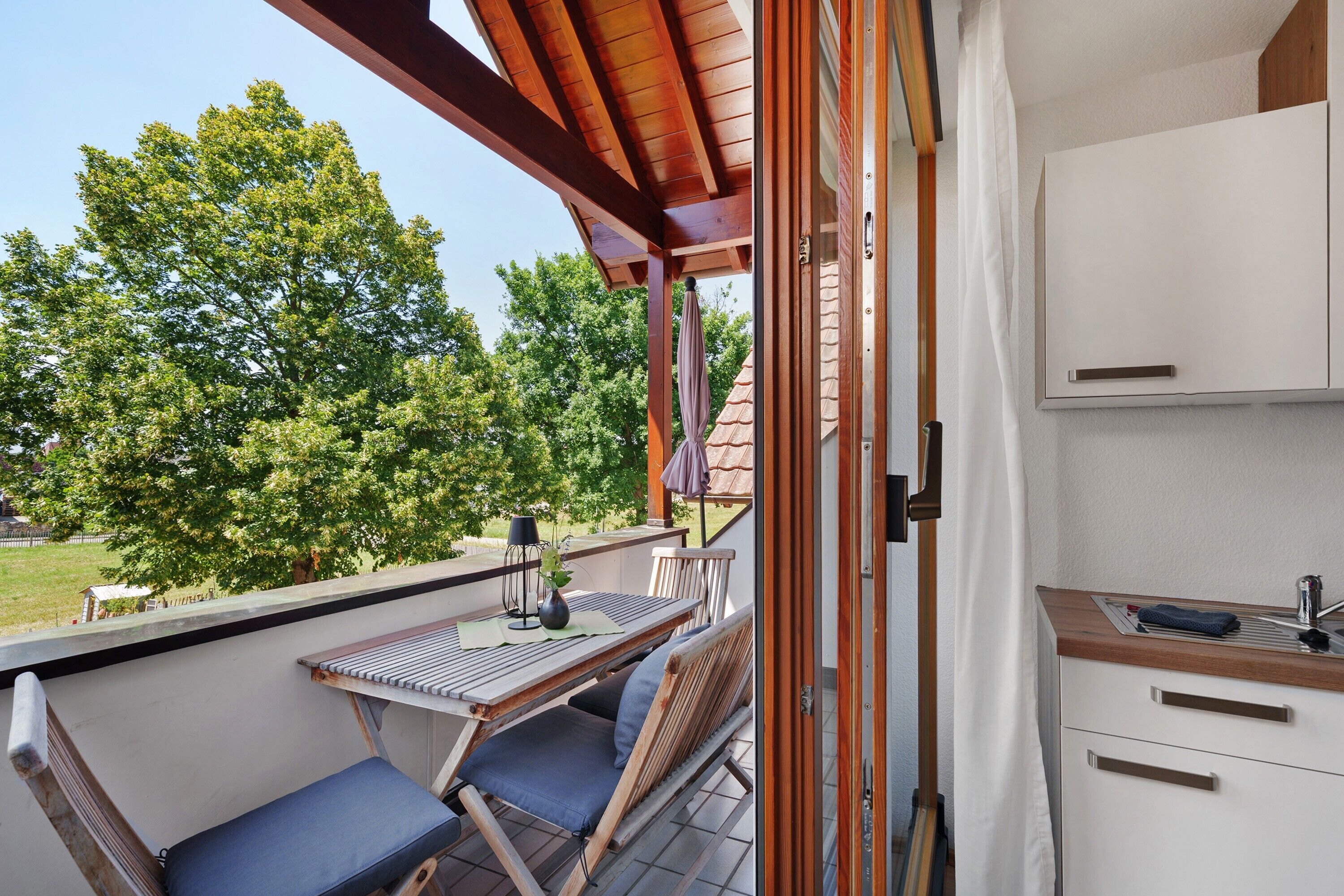 A balcony with a table and chairs, a view of trees, and a kitchen area with cabinets and a countertop.