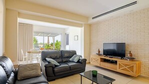 A modern living room with a leather sofa, a glass coffee table, and a TV on a wooden stand. - Gugel Waves Seaview 4BR Family Aparts (Nahariya)