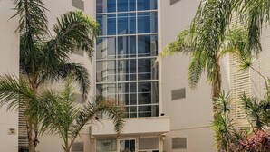 A modern building with a glass facade, surrounded by palm trees and potted plants. - Gugel Waves Seaview 4BR Family Aparts (Nahariya)