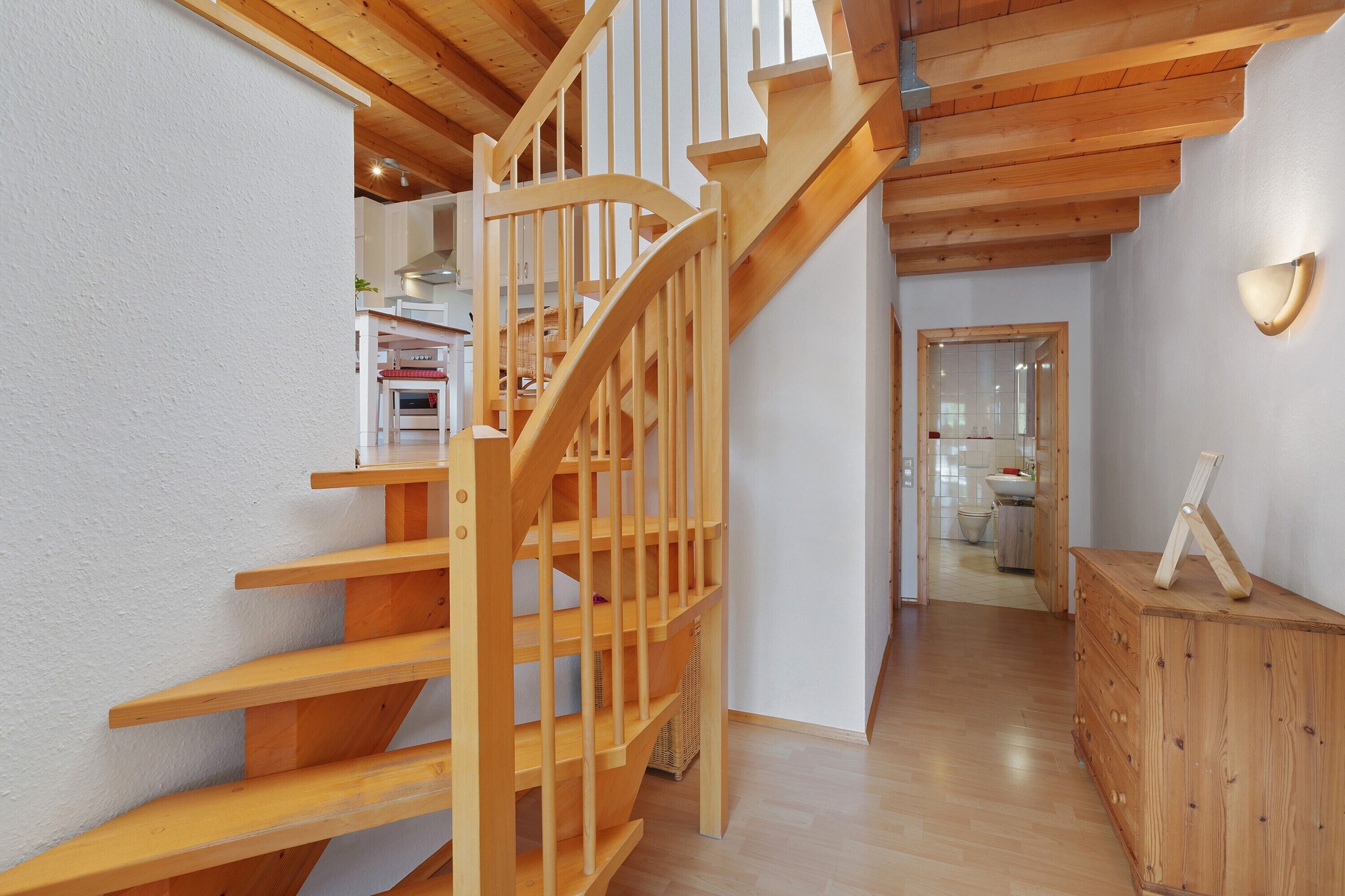 A wooden staircase leading to a second floor, a wooden dresser, and a kitchen area in the background.