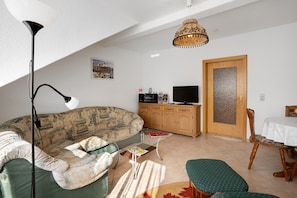 Uma sala de estar com sofá, mesa de centro, televisão, armário e área de jantar com mesa e cadeiras.