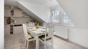 A dining area with a table set for four, white chairs, a window with a view, and a kitchen in the background. - Apartment 'Annemarie Galle' with Wi-Fi (Meißen)