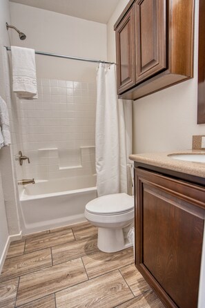 A bathroom with a bathtub, toilet, and wooden cabinets. - River Sands RV Resort (Ehrenberg)
