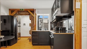 Une cuisine moderne avec des meubles de couleur sombre, un plancher en bois et un mur d’accent en pierre.