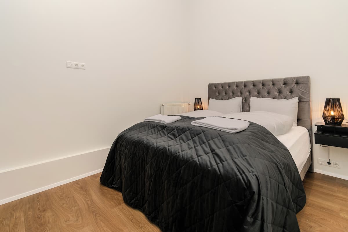 Un dormitorio con cama, paredes blancas y suelo de madera.