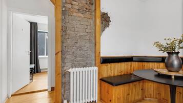 A room with a wooden bench, a radiator, and a vase with dried flowers on a table.