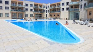 Ein Swimmingpool mit Liegestühlen und ein Gebäude mit Balkonen im Hintergrund.
