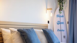 Ein Bett mit weißen und blauen Kissen, ein Surfbrett mit Schriftzug und eine wandmontierte Leuchte.